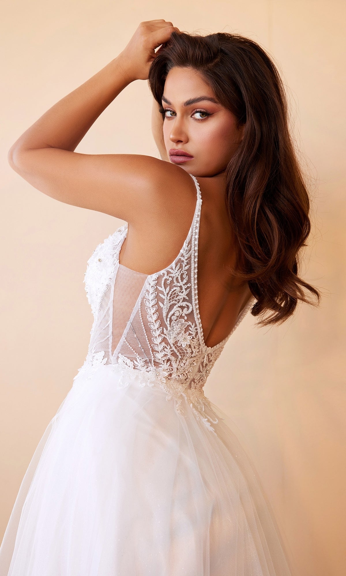 Woman in a Sheer-Bodice Long White Ball Gown CD0195W with a sleeveless design and sheer lace back looks over her shoulder against a neutral background.